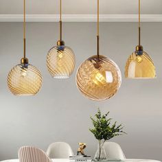 three glass globe lights hang over a dining room table with white chairs and a vase filled with flowers