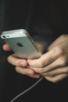 a person holding an iphone in their hands with ear buds attached to the back of it