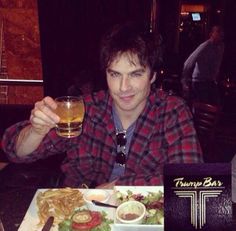 a man sitting at a table with a glass of beer in his hand and food on the plate