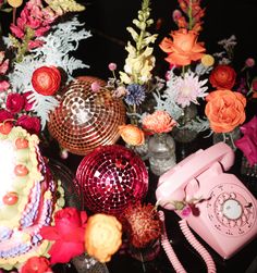 an assortment of decorative objects including a pink phone and flowers on a black table top