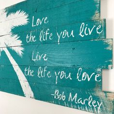 a wooden sign that says live the life you love with palm trees and bob marley