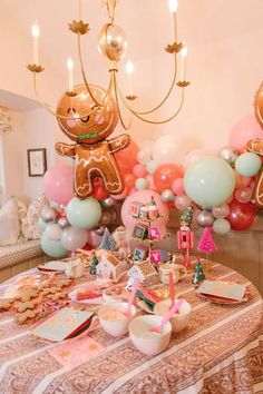 a table topped with lots of balloons and gingerbreads on top of it next to a chandelier