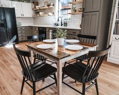 the kitchen table is set for four with plates and bowls on it, along with black chairs