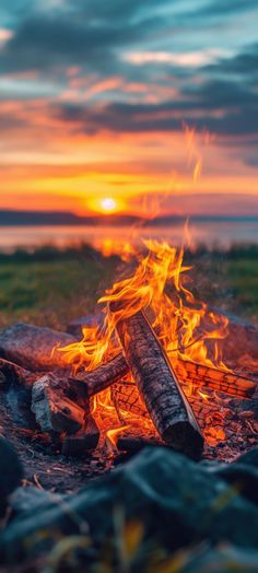 a campfire with the sun setting in the background and some logs on the ground