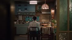 a woman sitting at a table in a kitchen next to a window with the light on