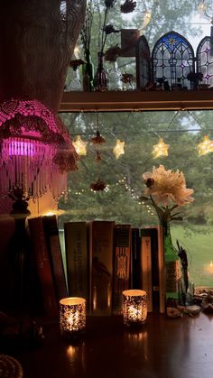 candles are lit in front of books on a window sill with flowers and other decorations