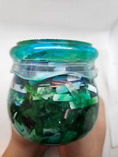 a hand holding a glass jar filled with green and blue items