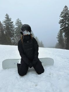 a person sitting in the snow with a snowboard on their feet and wearing a ski mask