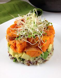 a white plate topped with an avocado and carrot salad covered in sprouts