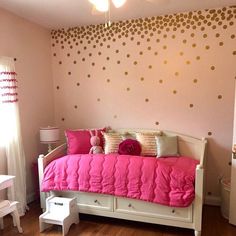 a pink and gold bedroom with polka dots on the wall, white dressers and bed