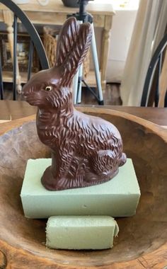 a chocolate bunny sitting on top of a piece of green soap next to a wooden bowl