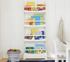 a white book shelf filled with books next to a blue rug and a bucket full of children's books