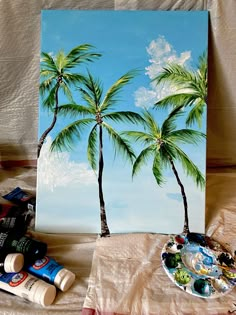 a painting with two palm trees on it next to some paint and other art supplies