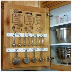 a wooden cabinet with measuring spoons and measuring cups on the bottom, labeled kitchen utensils