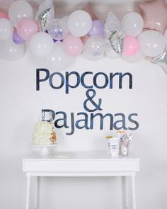 a white table topped with lots of balloons next to a sign that says popcorn and pajamas