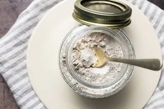 a jar filled with powder sitting on top of a white plate next to a spoon