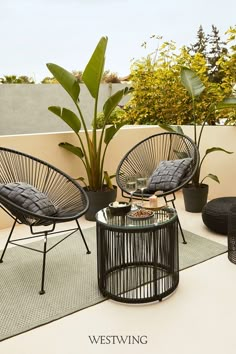 two wicker chairs sitting on top of a patio next to a table and potted plant