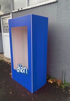 a blue box sitting in front of a building with the word den written on it