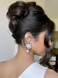 a woman in a white dress with her hair pulled back into a low bun and wearing earrings