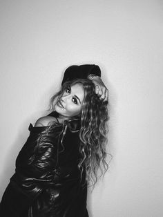 a black and white photo of a woman with long hair wearing a leather jacket, hat and boots