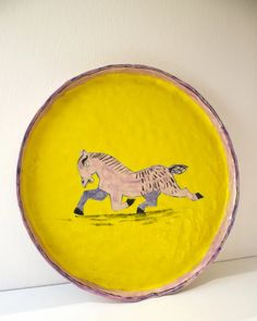 a yellow plate with a drawing of a horse on the front and side, against a white wall