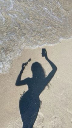 a shadow of a woman on the beach with a cell phone in her right hand