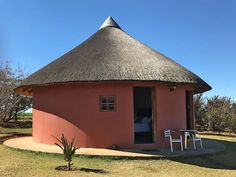 a small hut with a thatched roof and two chairs in the grass near it