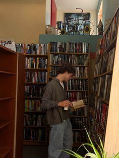 a young man reading a book in front of a bookshelf