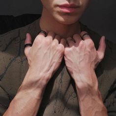 a man with his hands on his chest looking at the camera while wearing two rings