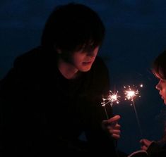 two people holding sparklers in their hands at the same time as they look at each other