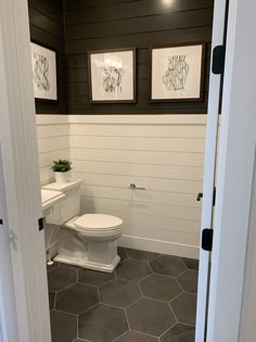 a white toilet sitting inside of a bathroom next to two pictures on the wall above it