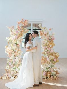 a man and woman standing in front of a floral arch with flowers on it's sides