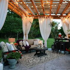 an outdoor living area with couches, tables and lights hanging from the pergolated roof