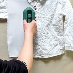 a person is holding an object in front of a white shirt on a hanger