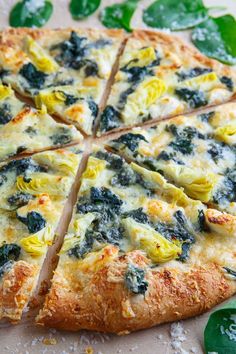 a pizza with spinach and cheese cut into eight slices on a table next to green leaves