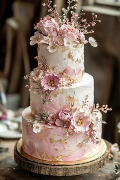 a three tiered wedding cake with pink flowers on the top and gold trimmings