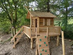 a wooden play structure with a slide and climbing frame in the sand near some trees