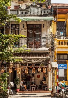 two people sitting at a table in front of a yellow building with balconies