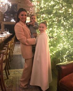 a woman and two children standing in front of a christmas tree with lights on it