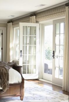 a bedroom with french doors and a bed in the middle, surrounded by beige curtains