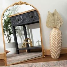 a mirror sitting on top of a wooden floor next to a vase