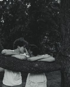 black and white photograph of two people embracing each other on a tree branch in the woods