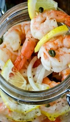 a glass jar filled with shrimp and lemon wedges