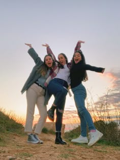 three young women are posing for the camera on a hill at sunset with their arms in the air