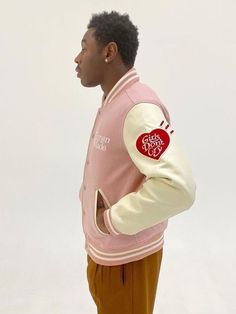 a man wearing a pink and white jacket with an apple patch on the sleeve, standing in front of a white background