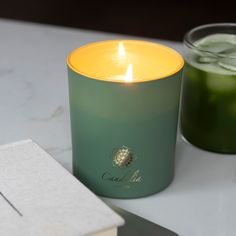 a candle sitting on top of a white table next to a book and glass filled with liquid