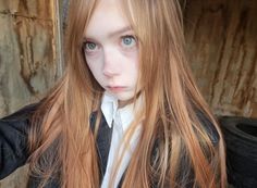 a girl with long red hair and blue eyes posing for the camera in front of a wooden wall