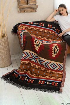 a woman sitting on top of a bed covered in a brown and red blanket next to a plant