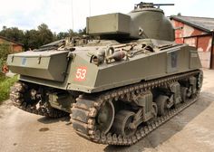 an army tank sitting on top of a dirt road next to a building and trees