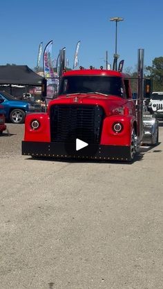 a red semi truck parked in a parking lot next to other cars and trucks behind it